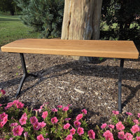 Garden bench by Treeboard with white oak seat and cast-iron legs, surrounded by flowers and a tree trunk.