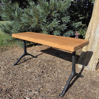 Garden bench by Treeboard with white oak seat and cast-iron legs, with a pine tree behind.