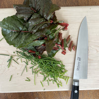 A Misono gyuto chef's knife from the molybdenum 440 series on a cutting board by Treeboard with chives and chard.
