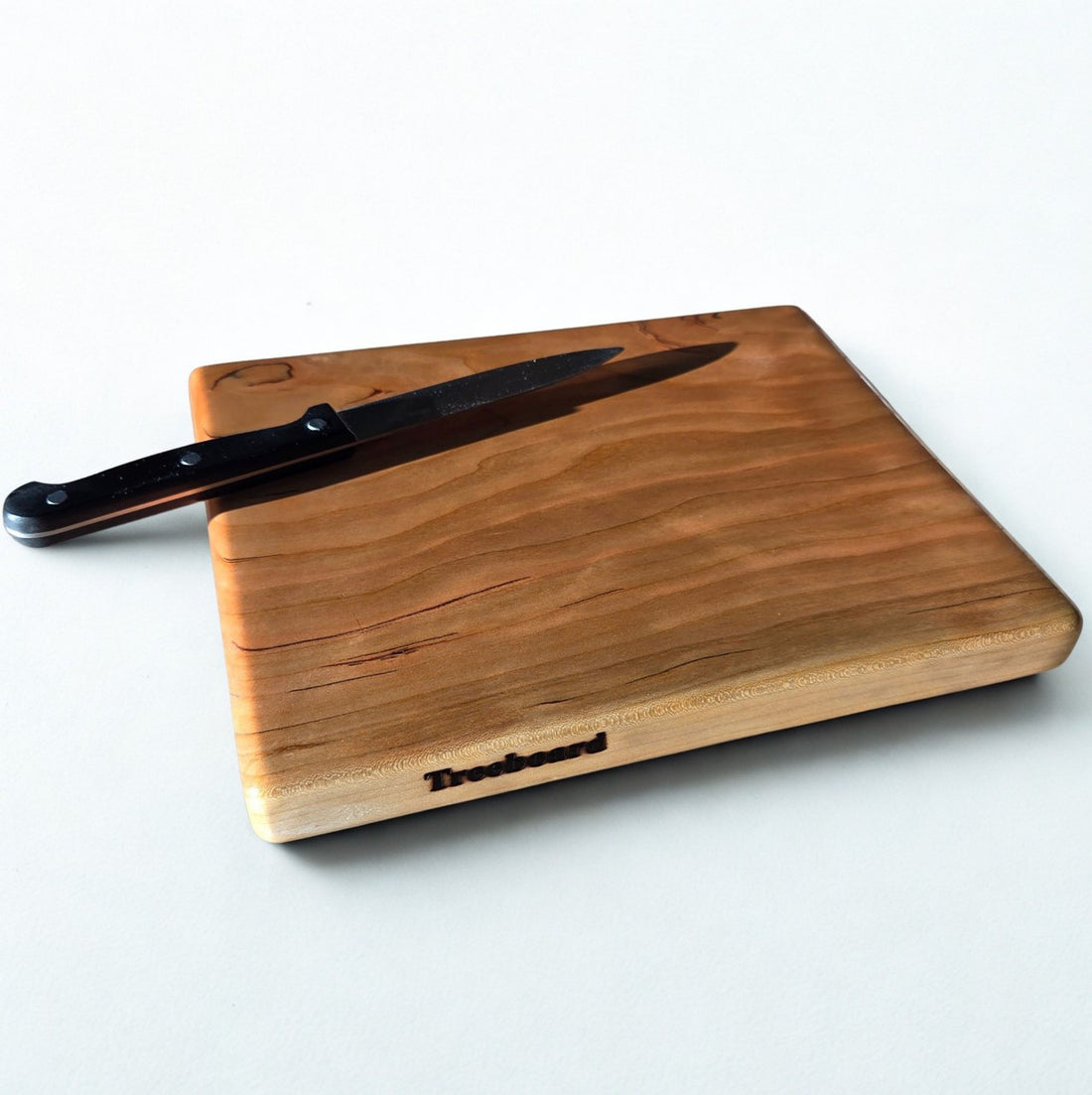 Small cherry cutting board by Treeboard with knife. Elegant chopping board with a white background. The black cherry is a "gummy" or "heavy gum" cherry.