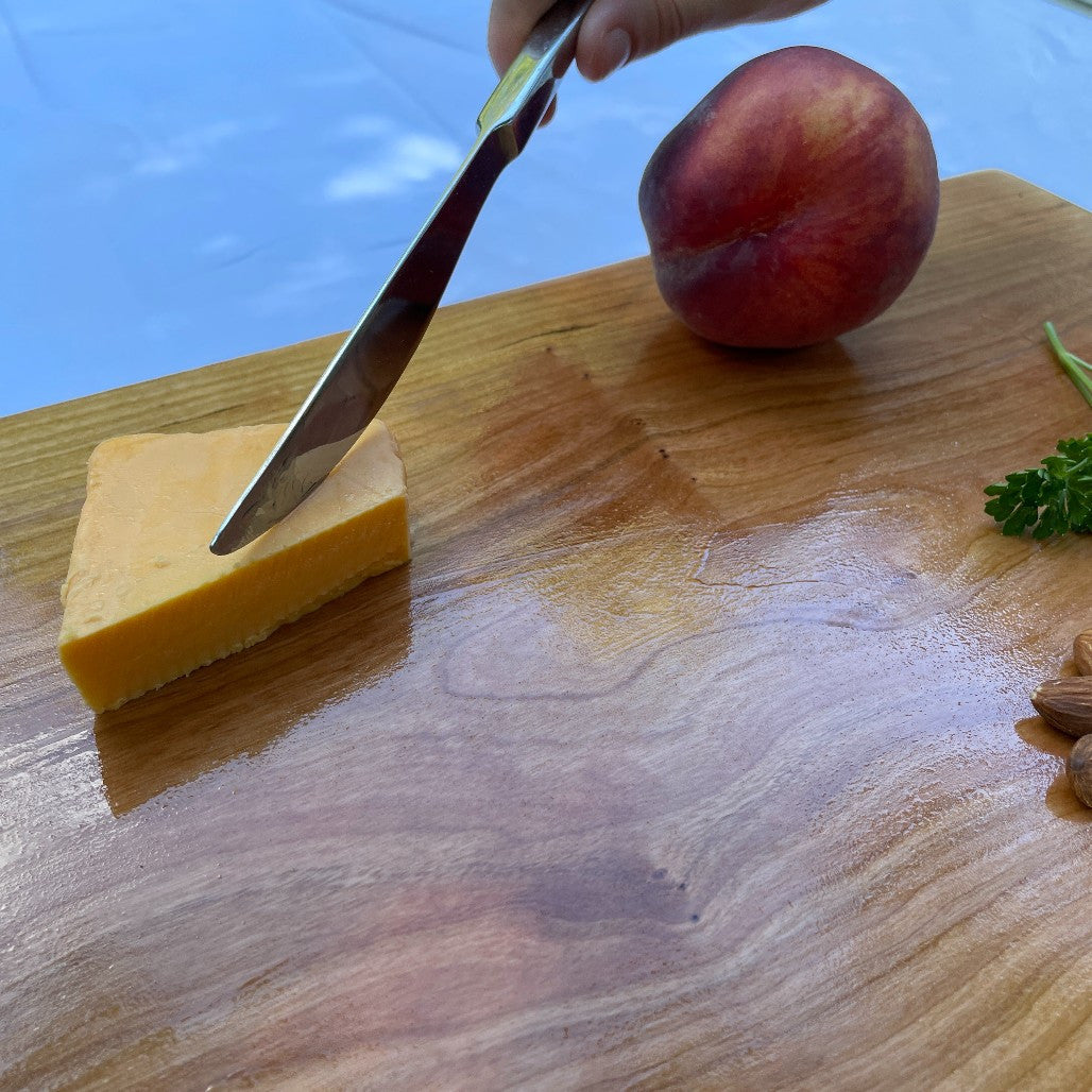 Large black cherry serving board and cutting board by Treeboard with cheddar cheese, knife and hand.