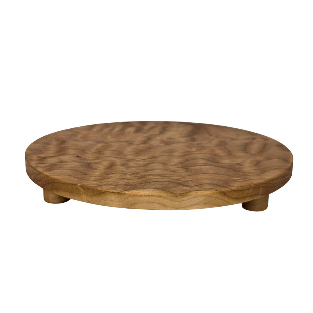 Round trivet seen from the side. A cherry stand for hot pans with three legs, by Treeboard. Photo shows curly cherry grain.